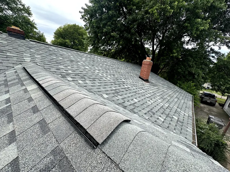 New architectural shingle roof with ridge vent beside a brick chimney